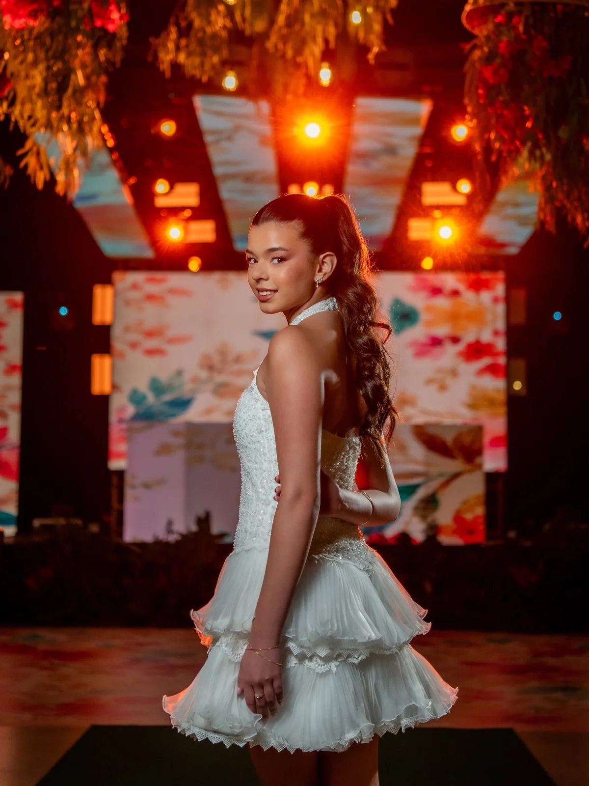 Quinceañera con vestido blanco corto bajo luces rojas en su fiesta