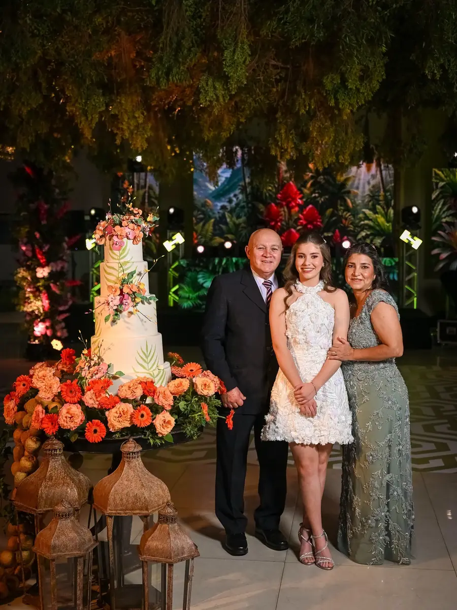 Quinceañera con sus papás junto a la torta y las flores